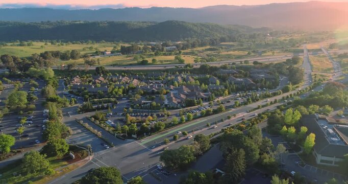 Aerial view of Sandhill Roa , Menlo Park. Silicon Valley, California, USA, at sunset. Cars travel on roads near office buildings and parking lots, with mountains in the background.