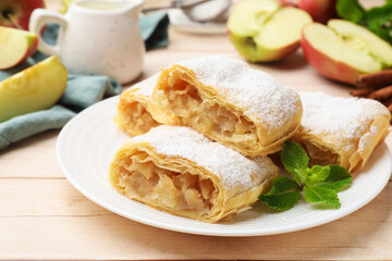 Pieces of tasty apple strudel with powdered sugar and mint on light wooden table, closeup