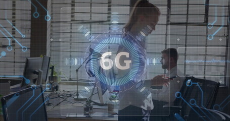 Gesturing businesswoman presenting 6G interface in modern office, with multiple monitors