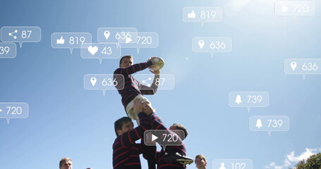 Jumping rugby jumper catching rugby ball on grassy pitch under blue sky, with striped jerseys