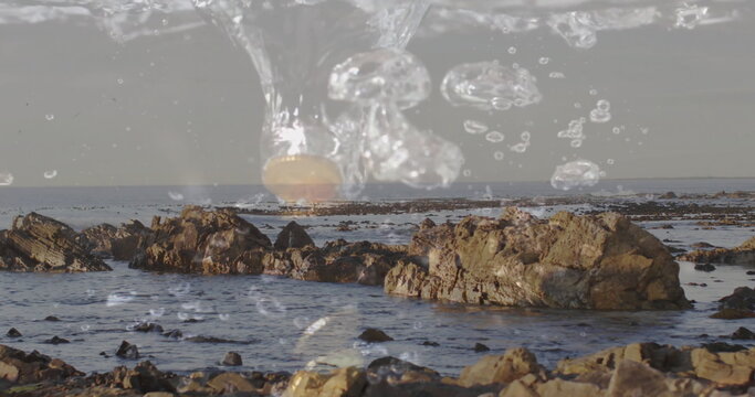 Fototapeta Showing jagged rocks rising from shallow water at seaside, with floating droplets and bubbles