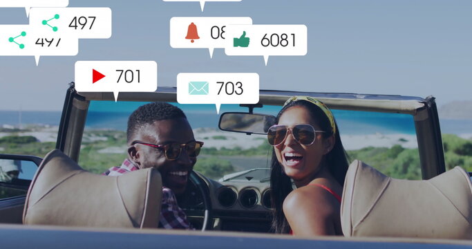 Sitting couple wearing sunglasses, viewing floating social icons in convertible car on coastal road - Powered by Adobe
