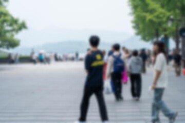 A blurred image of people walking in a city street. There is a man in the foreground with a backpack and a woman to the right with long hair.