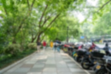 Blurry view of a paved path with green trees and foliage in Hangzhou, China. People and vehicles are barely visible.