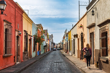 Adult female tourist walking along colorful colonial street in Santiago de Queretaro, Mexico