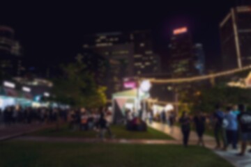 A blurred night scene in Hong Kong, China with bokeh lights in the background and many people walking in front of tall buildings.