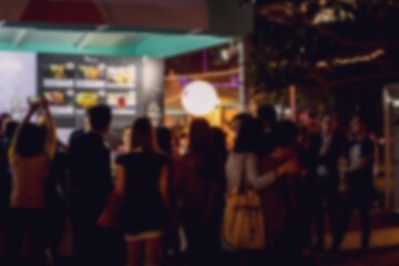 A blurred image of a crowd of people standing in front of a building in Hong Kong at night. The bokeh background suggests a bustling urban environment.