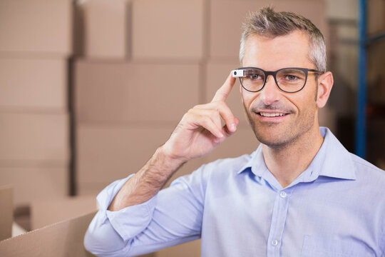 Middle-aged man pointing at smart glasses while packing cardboard boxes in warehouse, copy space