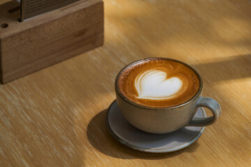 Obraz premium latte coffee art on wooden plate at desk in sun shine with shade of the tree