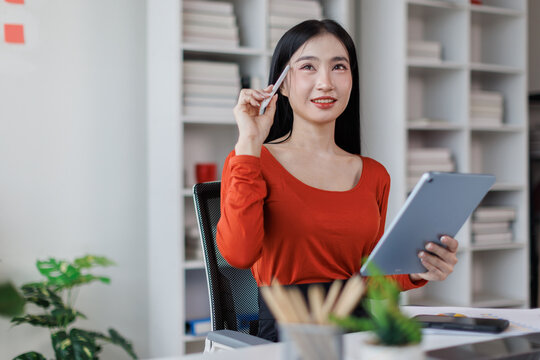 Asian Female business person using digital tablet and laptop or remote working at office, looking at digital tablet learning training, studying online thinking Financial and Accounting concept.
