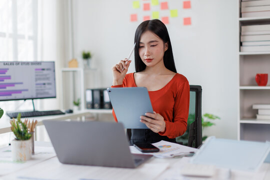 Asian Female business person using digital tablet and laptop or remote working at office, looking at digital tablet learning training, studying online thinking Financial and Accounting concept.
 - Powered by Adobe