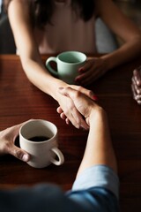 Close-up of a handshake of two people at a wooden table, both holding coffee cups. The handshake, coffee, and table are the main focus. Diverse individuals sharing coffee. Agreement through handshake.