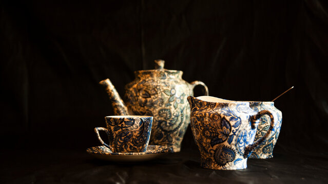 Vintage tea jug and cup used to serve dukes and duchesses, with the tea jug adorned with a beautiful pattern isolated in black background