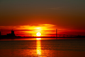 Detroit Ambassador Bridge connecting Canada and USA in the sunset, with the sun setting under the middle of the bridge.