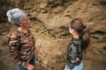 Mother and daughter dressed in hiking clothes, walking along a cliff observing cave paintings.