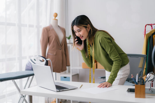 Fashion designer talking on phone and working on laptop in her studio - Powered by Adobe