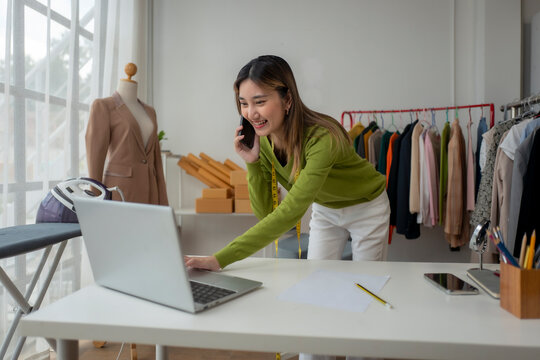 Asian fashion designer working on laptop and talking on phone in her studio