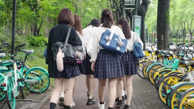 Slow-motion. Japanese high school girls in uniform walk on their school route chatting happily, surrounded by trees and buildings blending in harmony. Spring. Shanghai's Pudong New District. China.