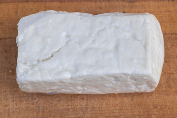 Block of crumbly white feta cheese on rustic wooden cutting board