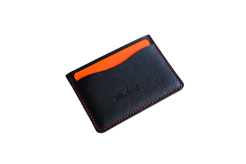 Sleek black leather card holder with vibrant orange card peeking out and subtle red stitching on a dark background.