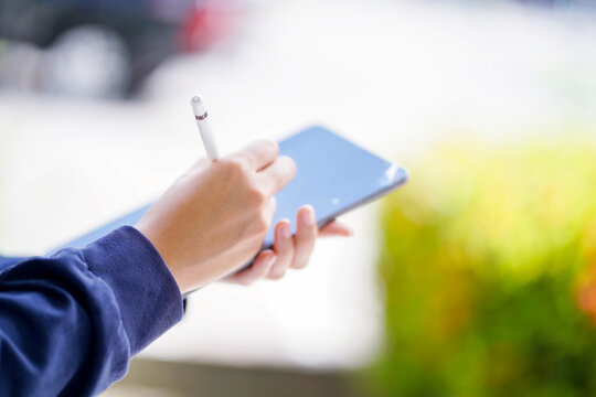 Closeup and crop hand of student in casual cloth make a short note on tablet on blurred background. Asian school concept.