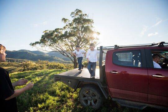 Happy kids jumping off back of ute to teenage boy in the Australian bush