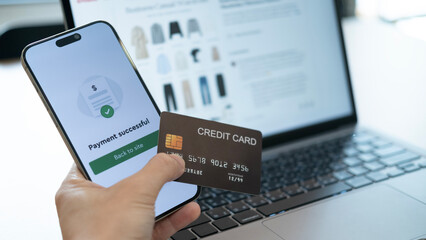 Holding a credit card with a phone screen saying “Payment successful” in front of a shopping website, symbolizing smooth spending in the digital era