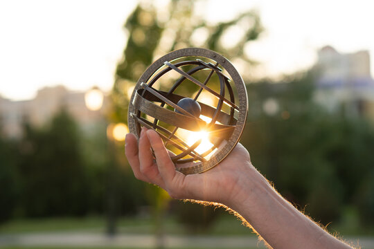 Extended arm holding antique globe illuminated by sunset rays. Armillary sphere astronomical instrument, spherical astrolabe
