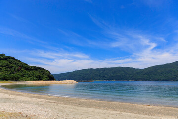 愛媛県伊方町、砂浜から望むムーンビーチ井野浦と防波堤、遠くに見える風車の夏景色

