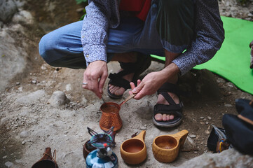 A candid scene of preparing a beverage outdoors using traditional copper tools and wooden cups. Captures the essence of exploration, camping, and connection with nature.
