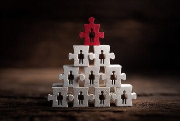 Pyramid structure made of puzzle pieces with human figures, topped by a red piece, representing teamwork and leadership