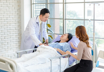 Obraz premium Asian man professional doctor visiting ward, consulting, talking to physician, senior woman patient lying on hospital bed explaining medical treatment with lovely daughter family showing care support.