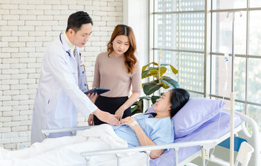 Fototapeta premium Asian man professional doctor visiting ward, consulting talking explaining medical treatment to lovely daughter family showing healthcare care support while senior woman patient lying on hospital bed.