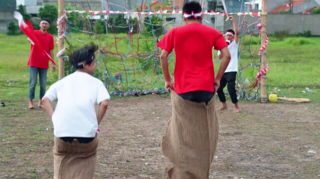 Young Indonesian Men In Sack Race, Fun Traditional Game For Independence Day Celebrations, Hopping Energetically Across The Field