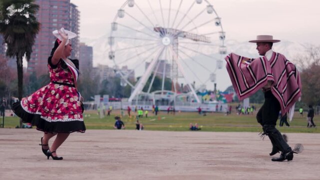 Smiling young couple dressed as Chilean huasos, joyfully dancing cueca outdoors. Traditional Chilean dance. Chilean traditions, celebrations.