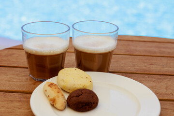Glasses of iced coffee and cookies near the pool on blurred nature background. Vacation, resort, summer, travel concept.