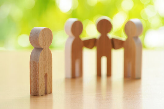 Wooden figure standing apart from a group of figures, symbolizing loneliness and exclusion