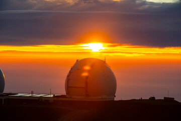 Obraz premium Astronomical observatories atop Mauna Kea, Hawaii, stand above the clouds at sunset, capturing a breathtaking view from one of the world’s premier stargazing locations.