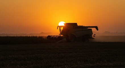 Naklejka premium Harvesting at Sunrise: Majestic Silhouette of a Combine Harvester