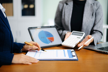 Two businesswomen review cash flow forecast and business growth charts on tablet and clipboard in office. Finance, data analytics, and planning concept for professionals.