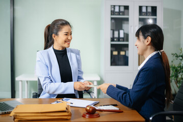 Two businesswomen in formal suits exchange cash over a contract document in an office. Bribery, fraud, and legal corruption concept with law props like gavel and folders.
