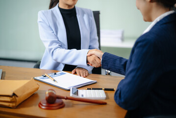 Two professional women shake hands over a signed contract at a legal office desk, symbolizing trust, agreement, and partnership.