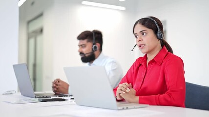 Diligent Indian businesswoman in red shirt and professional Indian businessman in white shirt focused on laptops, wearing headsets. Customer support, demonstrating efficiency in a modern office. - Powered by Adobe