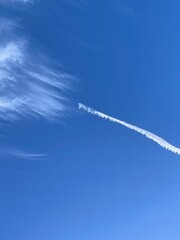 A white condensation trail left behind by an aircraft, seen cutting across a backdrop of blue sky...