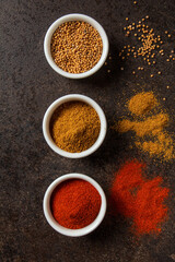 Flat lay of three colorful spice cups on a dark background for culinary inspiration