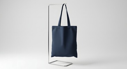 A navy blue tote bag hangs from a minimalist metal stand against a plain white background. totebag, tote bag, tote-bag mockup for design and fashion	
