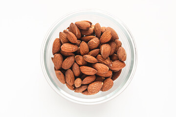 A pile of whole raw almonds in a clear bowl isolated on a clean white background. A simple, natural image representing healthy snacks and plant-based protein.