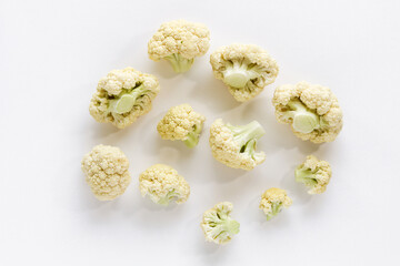 A scattering of fresh, raw cauliflower florets of various sizes, isolated on a clean white background, ready for cooking.