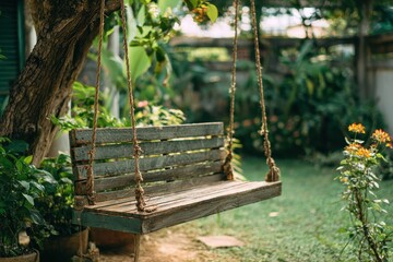 Naklejka premium Cozy wooden swing hanging from a tree with rope surrounded by lush greenery and vibrant flowers in a tranquil garden setting on a sunny day