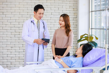 Obraz premium Asian man professional doctor visiting ward, consulting talking explaining medical treatment to lovely daughter family showing healthcare care support while senior woman patient lying on hospital bed.